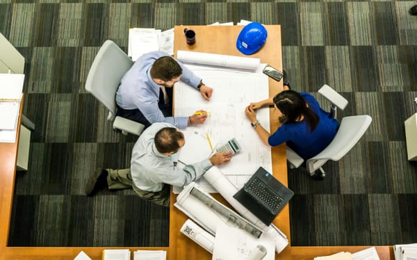 Three people in a meeting room working through documents spread out on a table, with a laptop to the side.